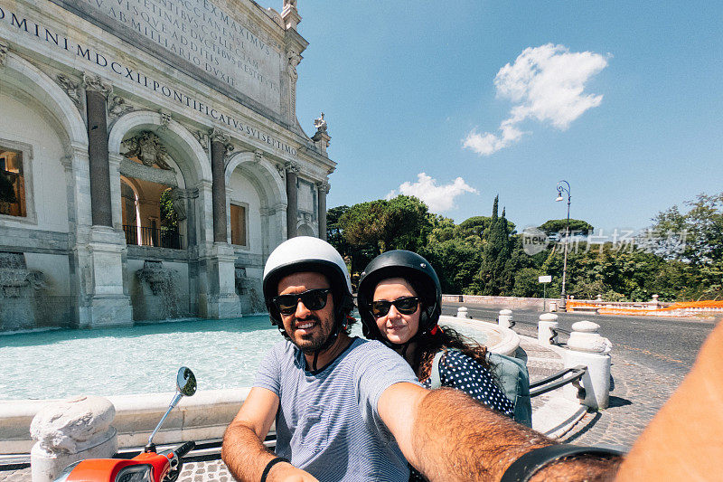 在意大利罗马Fontana dell'Acqua Paola前，一对年轻的成年夫妇骑着摩托车自拍
